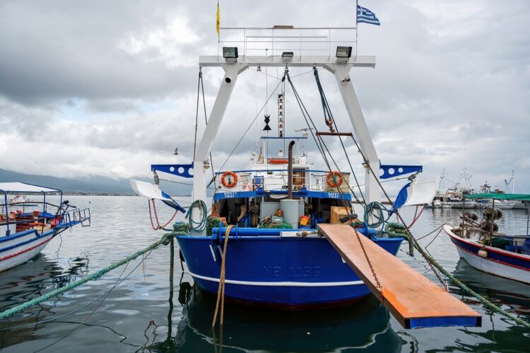 Moored blue and white boat with lowered bridge, made of metal near the shore of the Aegean sea, Stavros, Greece